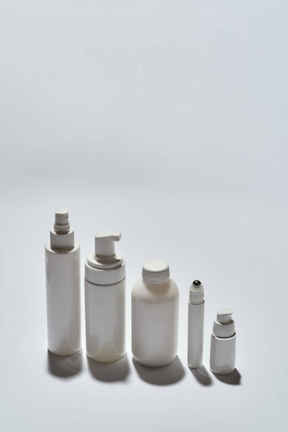 Different white bottles for beauty products arranged in the descending order of height isolated over white background with reflection - Foto, Bild