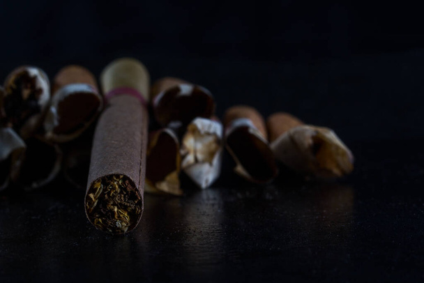 primer plano de un cigarrillo con tabaco en un fondo borroso de asquerosas y horribles colillas concepto de fumar y mal hábito - Foto, Imagen