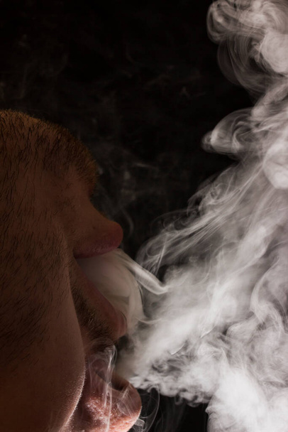 menee höyryä tupakoitsijan suusta pimeällä taustalla käsite nikotiiniriippuvuuden torjumisesta - Valokuva, kuva