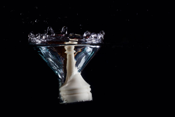 Beyaz satranç piyonu suya düştü ve su yüzeyinde güzel bir sıçrama yarattı. Karanlık bir arka plan kavramı olan masa oyunları ve iş dünyası üzerine. - Fotoğraf, Görsel