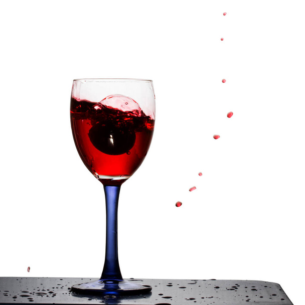 брызги красного вина в стакан с виноградом яркие летящие капли на белом фоне - Фото, изображение