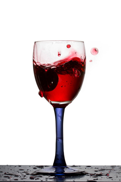 copa alta de vino tinto en la que las uvas caídas formaban un hermoso chapoteo sobre un fondo blanco - Foto, Imagen