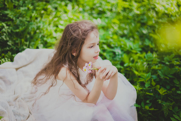 春の桜の庭で、ドレス姿の女の子がデイジーの花束を嗅ぎます - 写真・画像