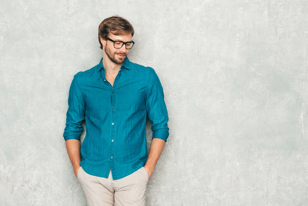 Portrait of handsome smiling hipster lumbersexual businessman model wearing casual jeans shirt clothes. Fashion stylish man posing against gray wall in studio in eyewear - Photo, image