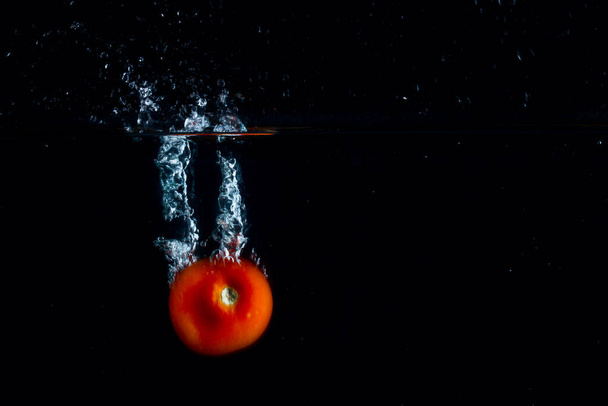 ripe red tomato falls to the bottom on a dark background while forming a beautiful splash of food concept - Photo, Image