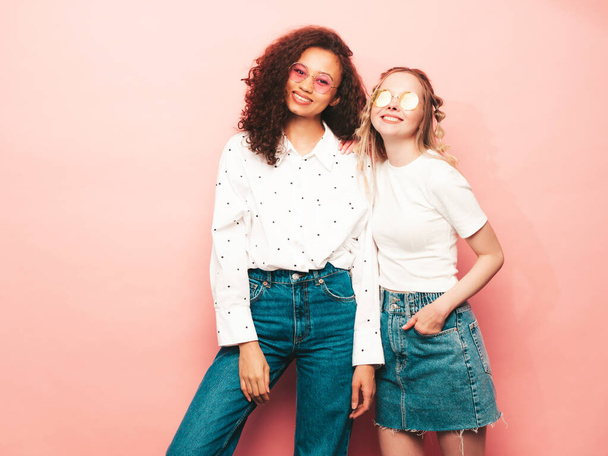 Two young beautiful smiling international hipster female in trendy summer clothes. Sexy carefree women posing near pink wall in studio. Positive models having fun. Concept of friendship - Fotoğraf, Görsel