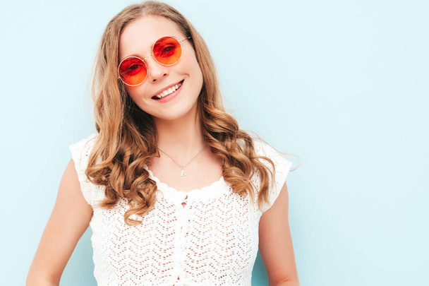 Portrait of young beautiful smiling female in trendy summer hipster clothes. Sexy carefree woman posing near light blue wall in studio. Positive model having fun indoors. In sunglasses - Foto, afbeelding