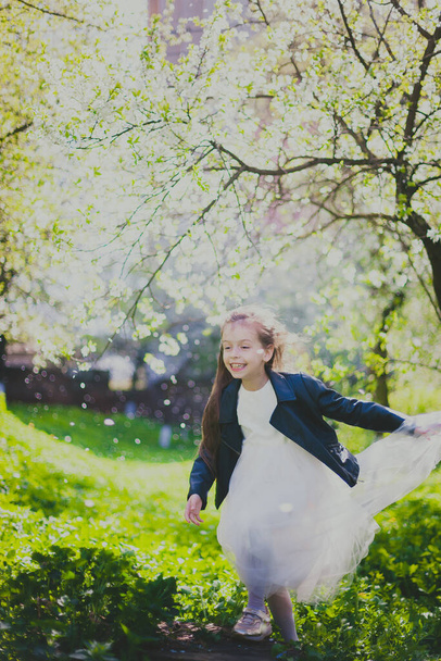 Siyah ceketli, beyaz elbiseli, bahar kiraz bahçesinde dans eden küçük kız. - Fotoğraf, Görsel