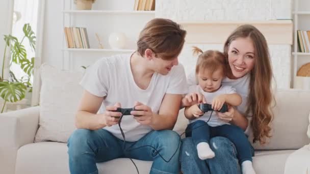 Νεαρή οικογένεια παιχνίδι online βίντεο παιχνίδι κάθεται στο σπίτι καναπέ καραντίνα αναψυχής, φροντίδα διασκεδαστικό γονείς μαμά και ο μπαμπάς καυκάσιος μητέρα και ο πατέρας διδάσκουν μικρό μωρό μικρή κόρη χαριτωμένο βρέφος παίζει κονσόλα - Πλάνα, βίντεο