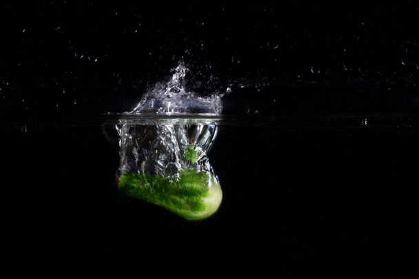 beautiful splash from a cucumber falling into the water on a dark background concept of food and vegetables - Foto, Bild