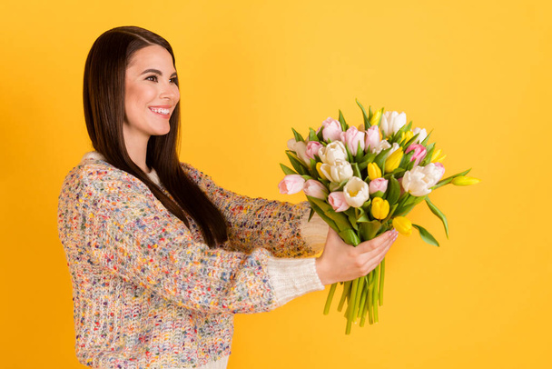 Foto del lado del perfil de la alegre dama feliz cogida de la mano tulipanes dan espacio vacío sonrisa aislada en el brillo de color amarillo fondo - Foto, Imagen