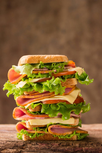 large shiny sandwich with ham cheese and greens on a wooden background looks very appetizing - Photo, image