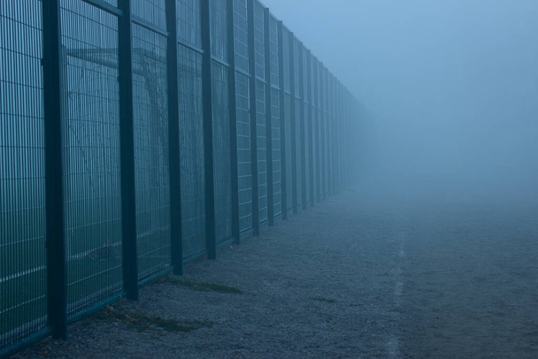 stade du soir couvert de brouillard épais clôture haute va dans la distance près de la piste de course le concept de la météo et le sport personne autour de l'atmosphère mystérieuse - Photo, image