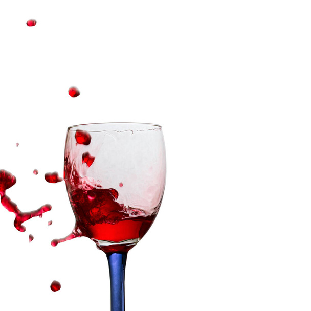 spektakularnie jasne krople czerwonego wina wylatujące ze szklanki na białym tle koncepcja popularnego napoju alkoholowego z winogron - Zdjęcie, obraz