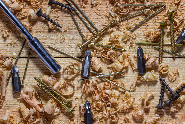 отвертка с различными насадками и крепежными ногтями и самонарезающими инструментами лежат на рабочем месте с тонкой промышленностью стружки древесины и концепцией обработки древесины - Фото, изображение