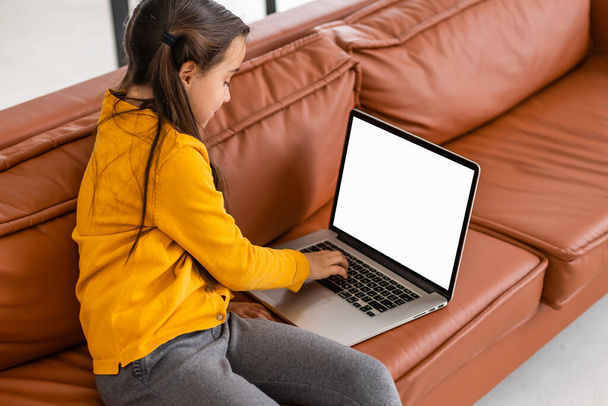距離学習。自宅の空白の画面でラップトップを使用して女の子のモックアップイメージ,コンピュータでオンライン学習,キッチンで机の上に座っている女性の子供とキーボードを入力します,リアビュー - 写真・画像