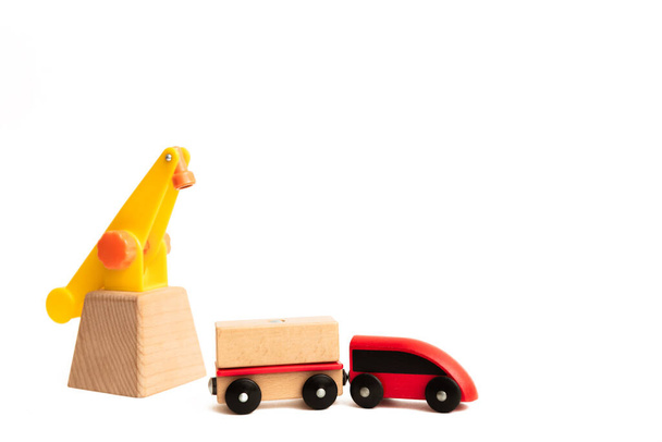 Toy wooden train and crane isolated on white background with copy space, text place. Red locomotive with a wagon. Baby play transport. Childhood. Environmentally friendly good. Toy shop or game store. - Fotó, kép