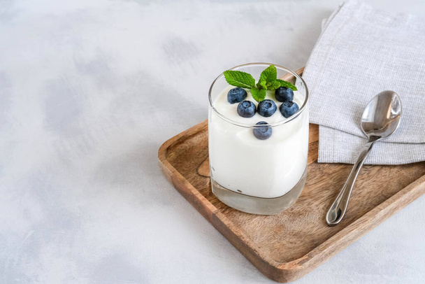 White yogurt in glass with fresh blueberry on a wooden tray. Homemade Greek yogurt in a glass - Foto, afbeelding