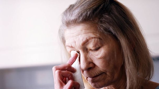 Καταθλιπτική γριά μοναχική γυναίκα σκουπίζει δάκρυα με ιστό ενώ κοιτάζει μέσα από το παράθυρο - Φωτογραφία, εικόνα