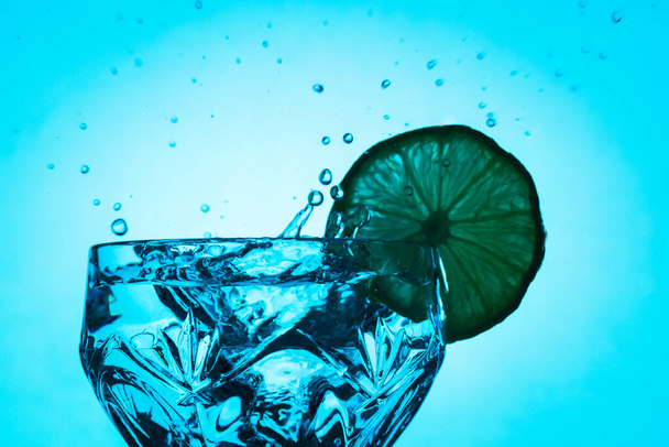bright splashes in a crystal glass with a slice of lemon on a light blue background - Photo, Image