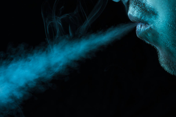man laat een jet van sigarettenrook op een donkere achtergrond concept van roken en slechte gewoonten - Foto, afbeelding