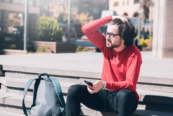 Ein junger Mann auf der Straße sitzt am Telefon - Foto, Bild