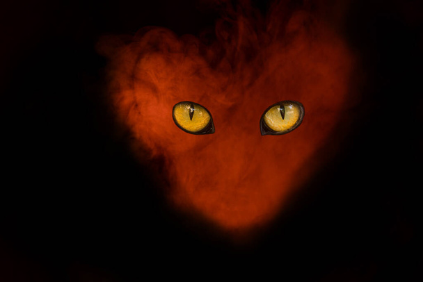 λαμπερό κεφάλι δαίμονα από ένα πορτοκαλί ατμό τσιγάρου σε ένα πορτρέτο σε σχήμα καρδιάς με μεγάλα μάτια την έννοια του καπνίσματος και του μυστικισμού - Φωτογραφία, εικόνα