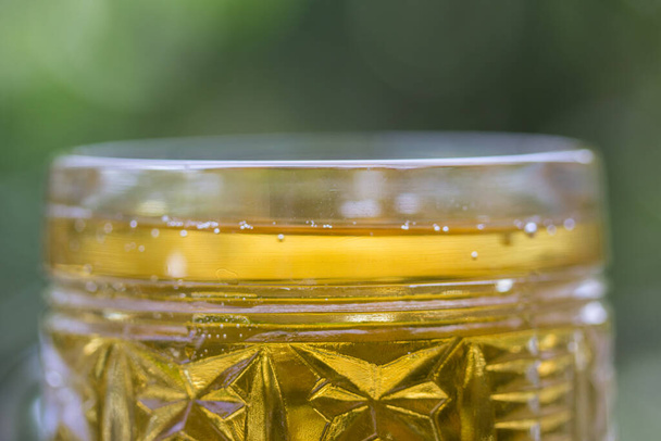 Alkolün yeşil yeşillik kavramının bulanık arka planında hafif birası olan kaliteli bir bardağın parlak tepesi. - Fotoğraf, Görsel