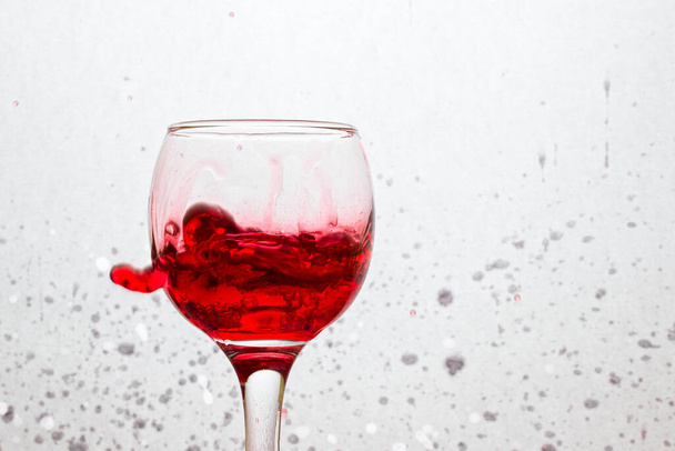 very bright wine splashing in a glass on a gray abstract background with spots from an alcoholic beverage - Foto, afbeelding