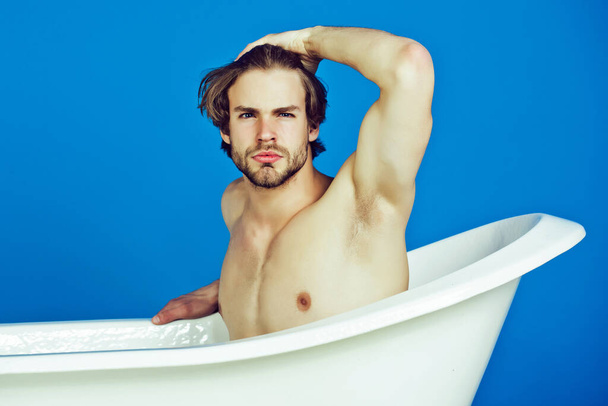 Young man with muscular body sitting in bath tub. Sexy man beauty, relax and hygiene, healthcare, copy space. - Fotó, kép
