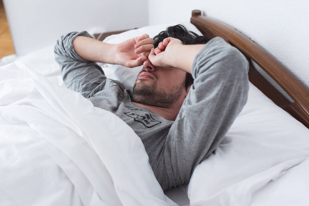 Hombre acostado en la cama, frotándose los ojos, estirándose por la mañana. Despertar por la mañana - Foto, imagen