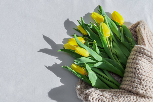 Um buquê de tulipas amarelas de primavera em um suéter de malha jaz à direita na cama com um lugar para texto à esquerda, uma vista superior de close-up. - Foto, Imagem