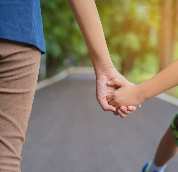 image of sister and brother holding hand while they walk on street in the park with green bokeh of tree in background. - Photo, Image