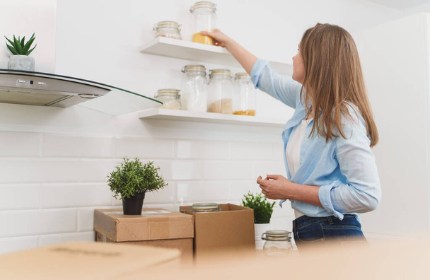 Mujer arregla utensilios de cocina después de mudarse a un nuevo apartamento. - Foto, Imagen