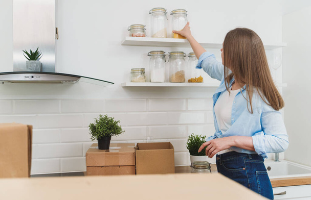 Женщина устраивает кухонную утварь после переезда в новую квартиру. - Фото, изображение