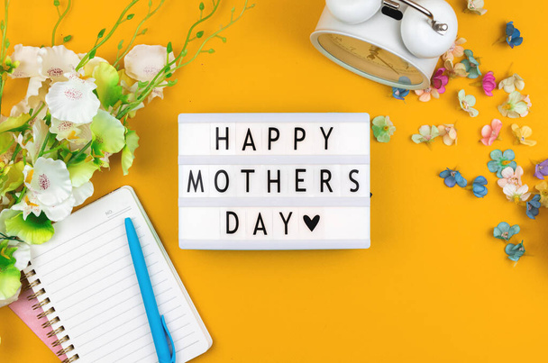 Happy Mothers Day text message on lightbox, greeting card flat lay concept with yellow background and spring flowers, top view - Фото, зображення