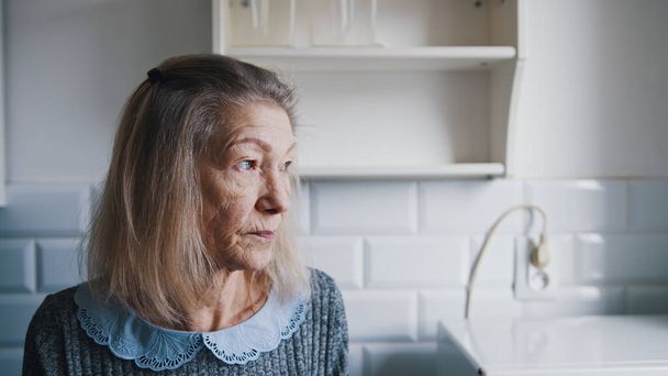 Triste anciana solitaria de pelo gris mirando por la ventana. Persona vulnerable en cuarentena - Foto, Imagen