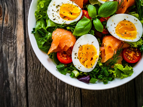 Salmon salad - smoked salmon hard boiled eggs and green vegetables on wooden table  - Photo, image