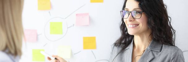 Business woman showing colleague with ballpoint pen stickers on chalkboard - Valokuva, kuva