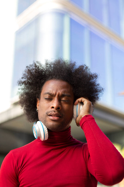 Portré fiatal fekete férfi afro frizurával zenét hallgat a szabadban. A szöveg helye.  - Fotó, kép