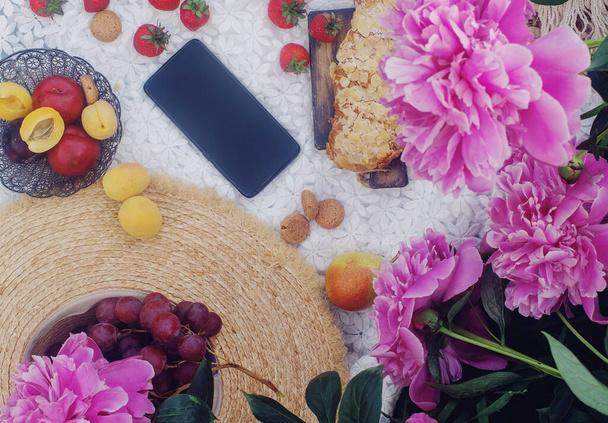 Picnic de verano al aire libre en estilo francés con frutas orgánicas frescas, flores de peonía, croissant de almendras en tela de lino blanco - Foto, imagen