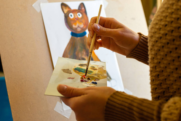 Porträt des Künstlers bei der Arbeit, die Hände eines Mädchens auf einer Palette mit einem Pinsel mischt Farben - Foto, Bild