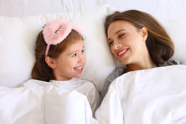From above delighted girl and and young woman smiling and looking at each other while lying under warm duvet in morning at home - Фото, зображення