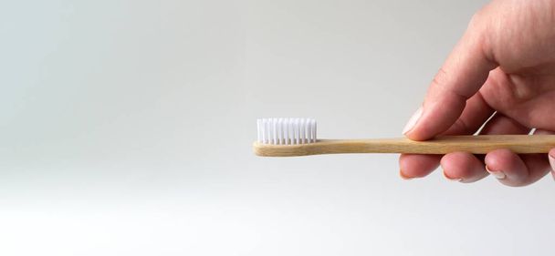 Uma mão feminina segura uma escova de dentes de bambu. Fundo Pastel. Conceito de material ecológico. Espaço para cópia. Orientação horizontal. Banca.  - Foto, Imagem