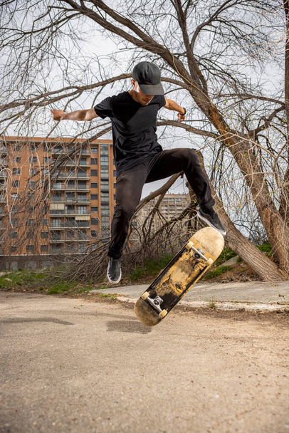 Jonge blanke man in een zwart shirt en pet springen met zijn skateboard - Foto, afbeelding