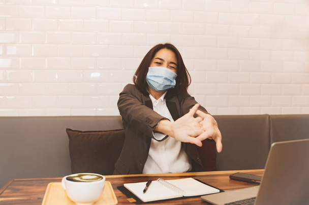 Mulher de negócios de meia-idade usando uma máscara, sentada em seus pulsos doendo de trabalho de negócios em um escritório, tem fadiga da síndrome do escritório em seus pulsos, ela se sente desconfortável. - Foto, Imagem