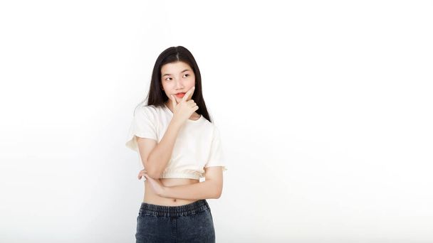 Привлекательная азиатка в нейтральной повседневной одежде, стоящая, думая на белом фоне с копировальным пространством - Фото, изображение