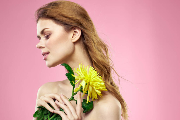 Beautiful girl with a yellow flower on a pink background nude shoulders makeup - Zdjęcie, obraz