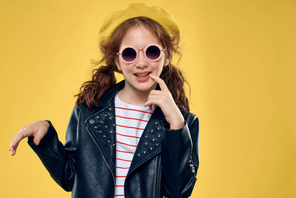 Cheerful little girl in sunglasses and hat lifestyle studio yellow background fashion - Zdjęcie, obraz