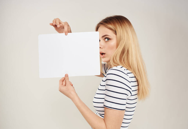 Mulher de t-shirt listrada cabelo loiro e uma folha branca de papel sobre um fundo bege - Foto, Imagem